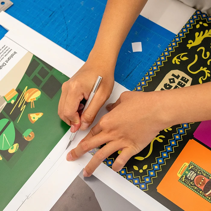 A student trims out a brightly colored poster design using a craft knife