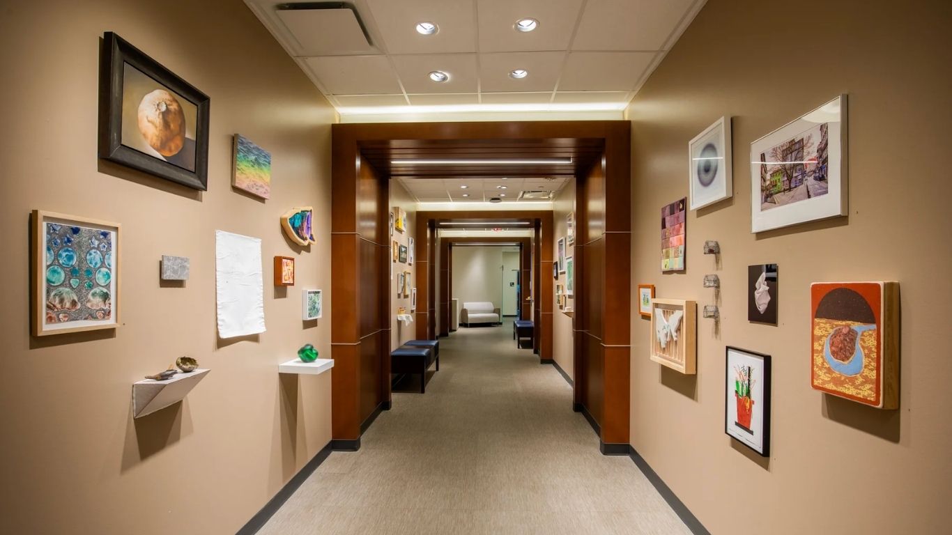 A hallway gallery at Moncrief Cancer Institute features an eclectic display of paintings, drawings, photographs, textiles and sculptural works installed along both walls as part of the Creative Care exhibition.
