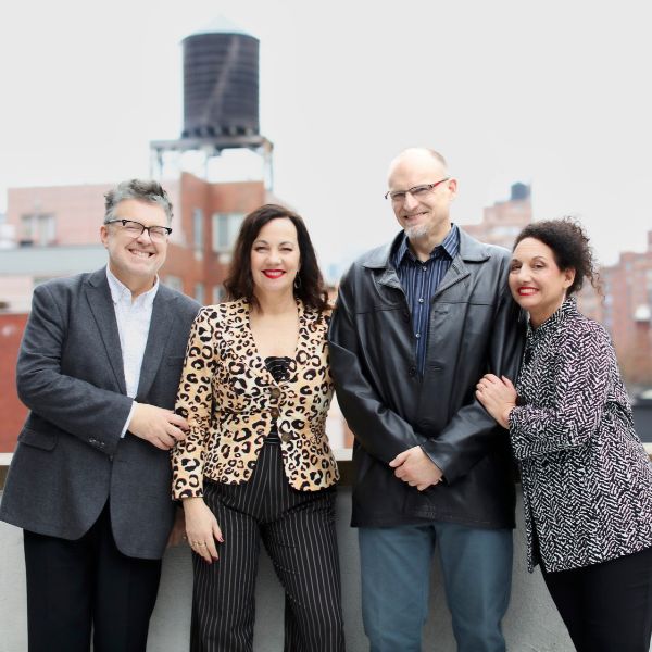 NY Voices NY Voices press release image of the group standing on a building roof with the cityscape behind them