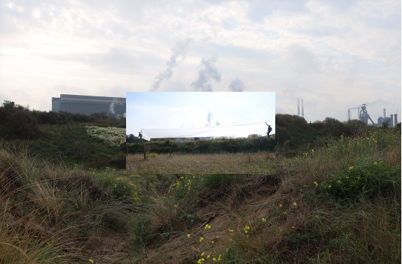 An industrial landscape with grassy terrain and distant factory structures beneath a cloudy sky. A smaller, brighter photograph is layered over the center, showing a performance involving a long white fabric installation.