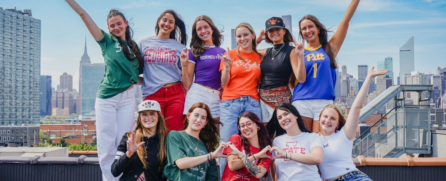 Ten CLASS: The NYC Experience participants representing different universities pose together on a rooftop overlooking the Manhattan skyline. Kirkland stands in the back row wearing a purple TCU Horned Frogs shirt and making the Horned Frog hand sign.