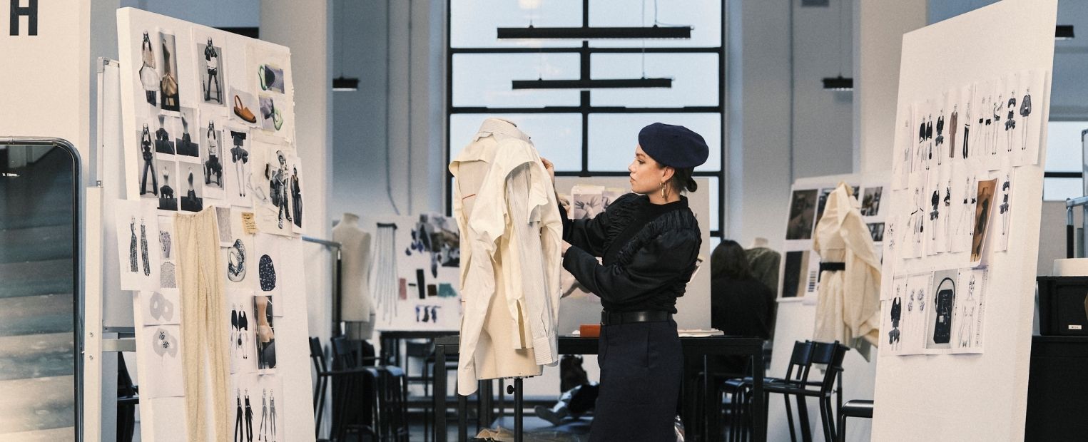 A Polimoda fashion student works on a garment in a design studio surrounded by fashion sketches, mood boards and works in progress.