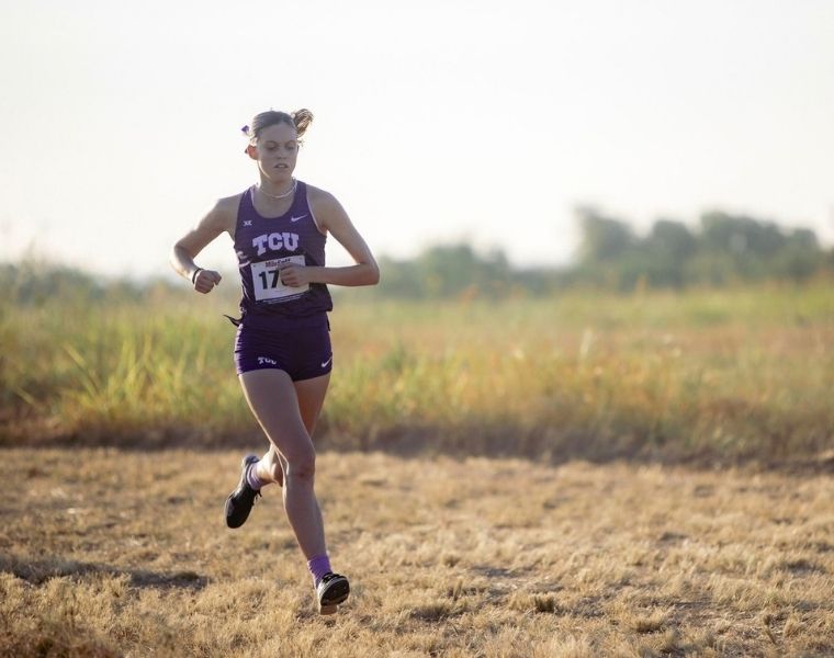 McKenzie Bailey runs across a grassy cross country course in a purple TCU uniform during a race.
