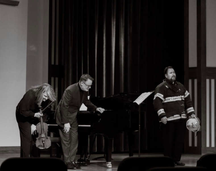Black-and-white panorama showing the performers’ curtain call. Dr. Ames Asbell bows with viola in hand, Dr. Joey Martin leans forward beside the piano, and Dr. Richard Novak, now wearing a fire fighter suit.