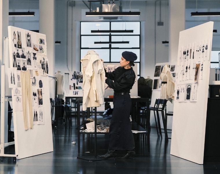 A Polimoda fashion student works on a garment in a design studio surrounded by fashion sketches, mood boards and works in progress.
