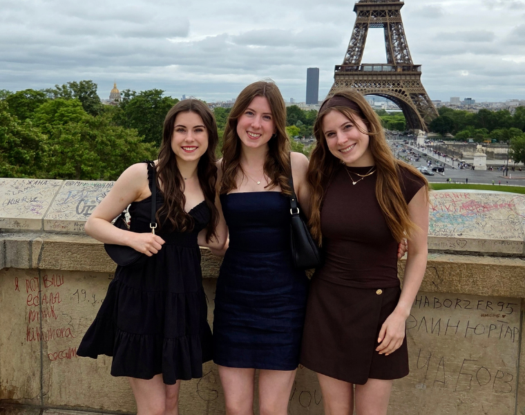 Victoria, Sasha and Katya Volodina stand together overlooking Paris, smiling with their arms around one another as the Eiffel Tower rises in the background.