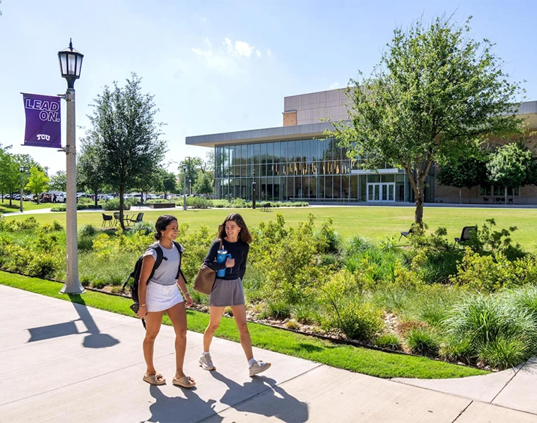 Two students chat as they walk along the Baker Martin Creative Commons, with the Boschini Music Center in the background