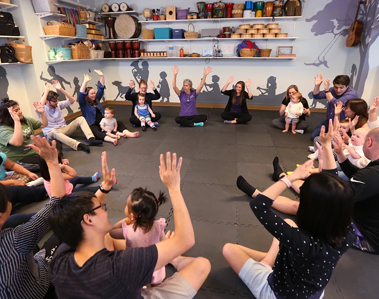 Parents and their children, seated in a circle, interact with the music instructor