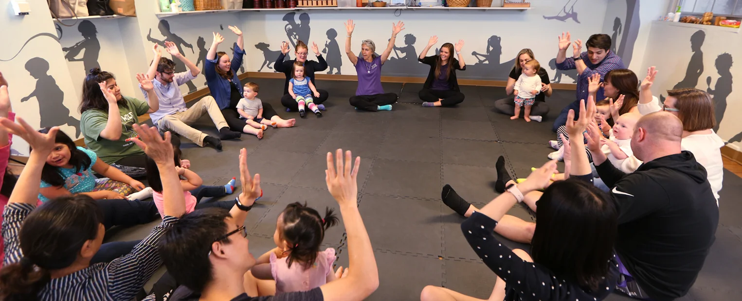 Parents and their children, seated in a circle, interact with the music instructor