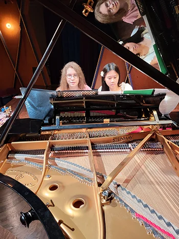 A piano instructor and her student, seated at a grand piano