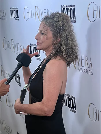 Suki John speaks into a microphone in front of a large Chita Rivera Awards backdrop