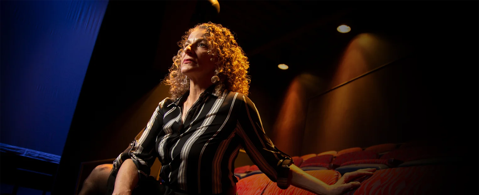 Suki John, seated in a theatre chair, looks off-camera