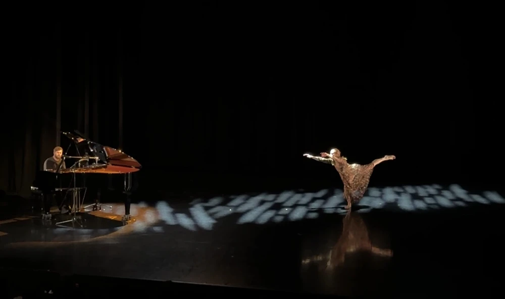 Sheaff  dances on a dark stage while Laboissiere plays on a nearby grand piano