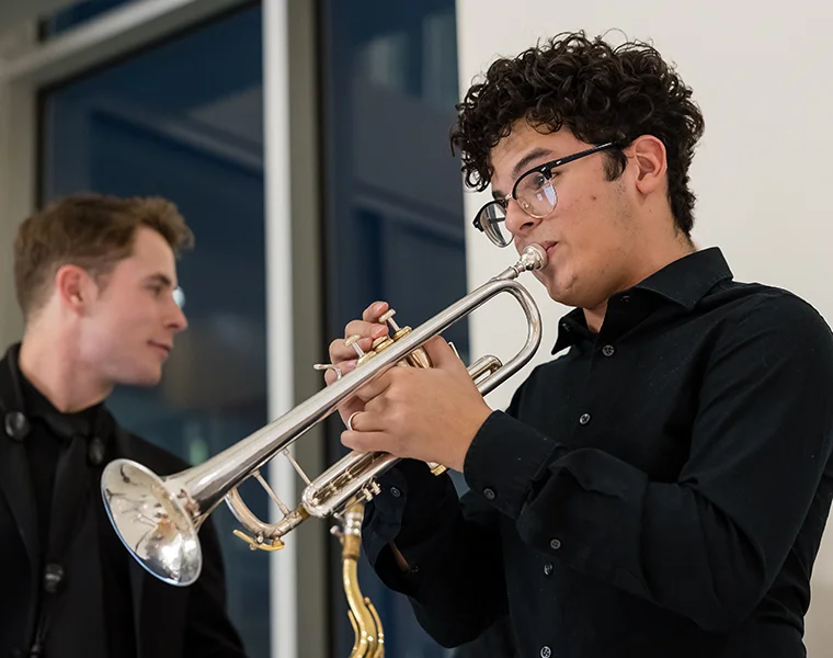 A student wearing a black shirt and glasses plays a silver trumpet