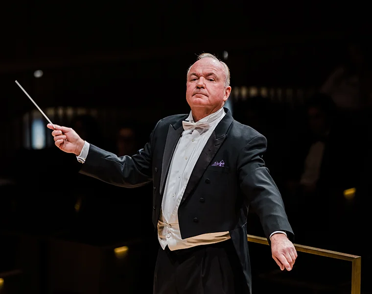 Bobby R. Francis, wearing a tuxedo, conducts the TCU Wind Symphony