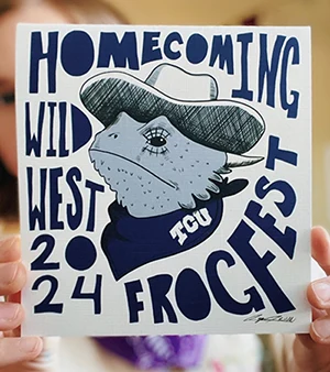 Caya holds up a copy of her poster: a horned frog in western attire with Homecoming Wild West 2024 Frogfest in hand-drawn lettering