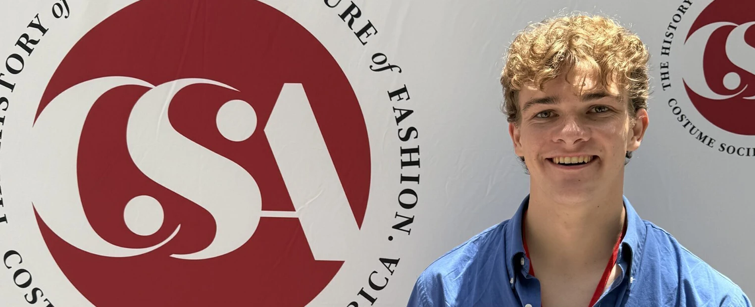 Henry Cawood hold award certificate in front of Costume Society of America backdrop