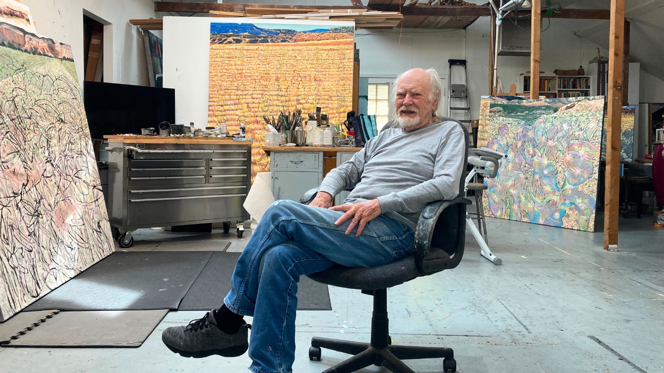 Jim Woodson sits relaxed in a swiveling office chair in the middle of a spacious, light-filled studio. Large finished canvases—abstracted, colorful landscapes—lean against the walls and stand on easels around him, while a stainless-steel tool