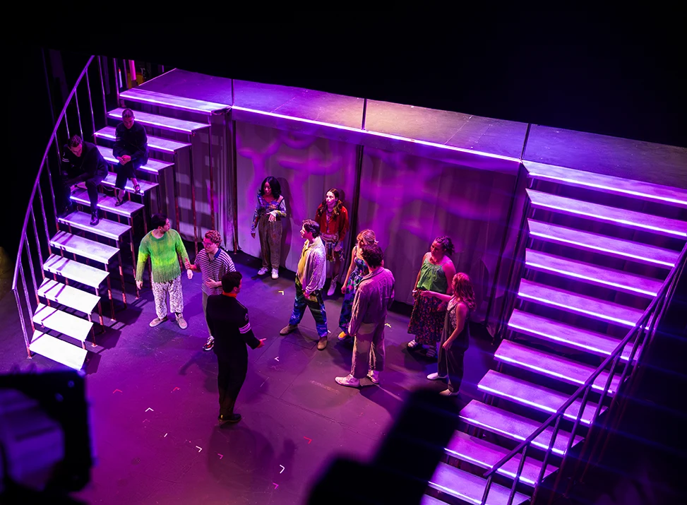 Birds-eye view of a dress rehearsal, with actors gathered on the first level of a two-tier stage set
