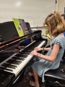 A young girl in a blue dress plays the piano.
