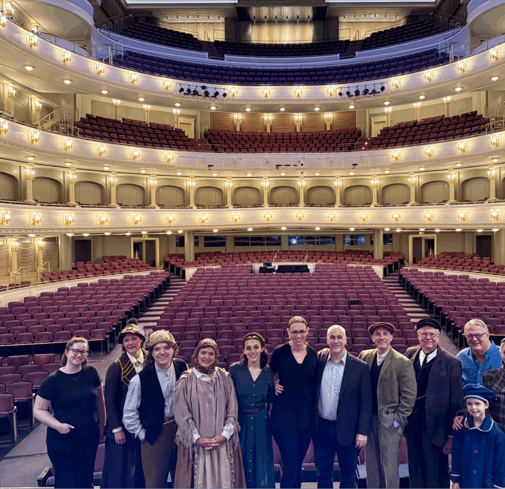 On the stage at Bass Hall with “Ellis Island: The Dream of America” cast.From left: Kaitlin Hatton (professional stage manager); Jennifer Engler (TCU theatre chair); Ethan Hyatt (current TCU student); Lana Hoover (professional actor); Lourdes Bradley (current TCU student); Stephanie Rhodes Russell (resident conductor of FW Symphony Orchestra); Peter Boyer (composer of “Ellis Island: The Dream of America”); Curtis Shideler (Theatre TCU alum); Alan Shorter (Theatre TCU faculty); Lucy Bennetch (child professional actor); Harry Parker (Theatre TCU faculty, director); Taylor Staniforth (Theatre TCU alum)
